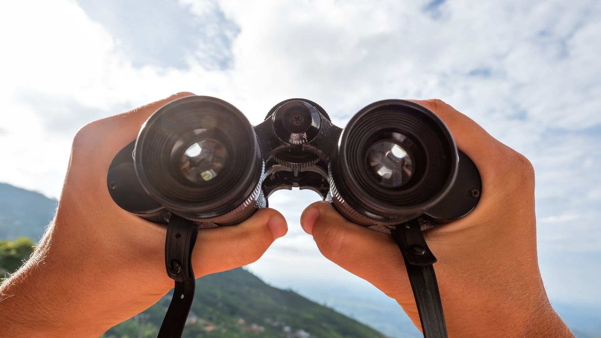 First-person view of hands holding binoculars up to a green mountain landscape