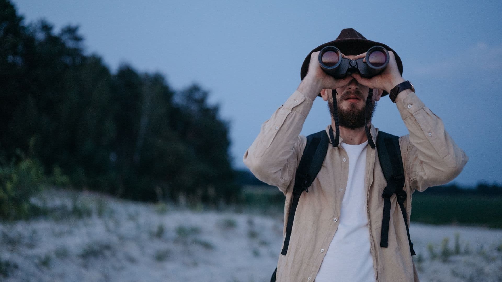 Un observateur au crépuscule, sac au dos, scrute l'horizon aux jumelles dans une lumière bleutée